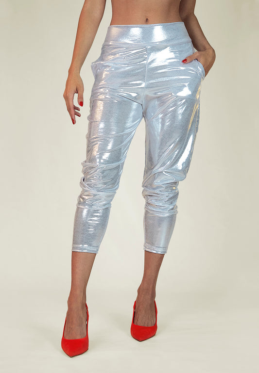 A woman wearing the platinum silver metallic slouch pants with a relaxed fit, mid-waist, with a shiny, reflective texture. The pants are styled in a way that they are slouched at the top and fitted at the bottom, showing off some skin at the upper calf area.